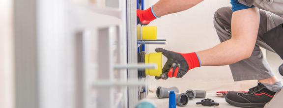 Gloved plumber working on pipes in the wall