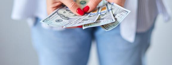 Woman with bright nail polish holding dollar bills in hand